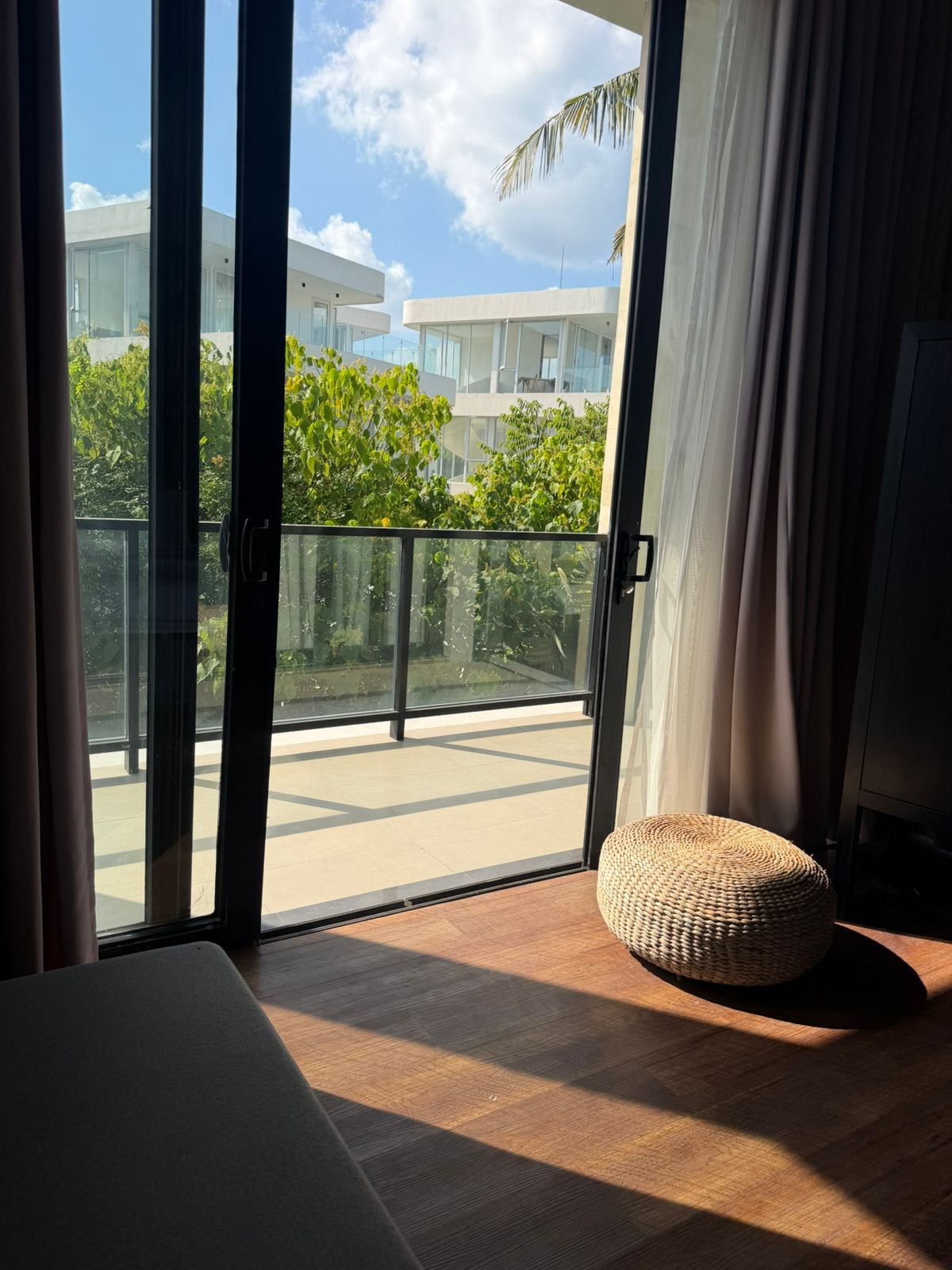 Ein Zimmer mit einer großen Glasschiebetür, die auf einen Balkon mit Blick auf ein Gebäude und Grünflächen führt.