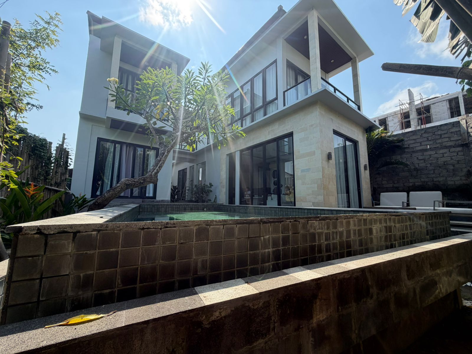 A modern two-story house with a swimming pool, large windows, and a stone wall.