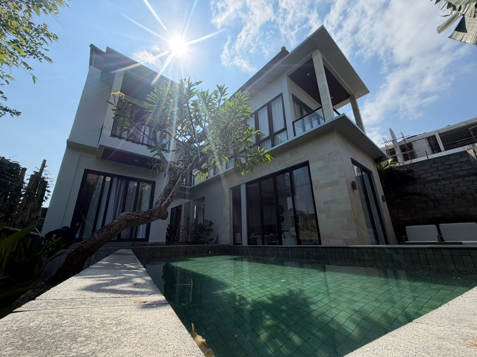 A modern two-story house with a swimming pool, large windows, and a clear sky.