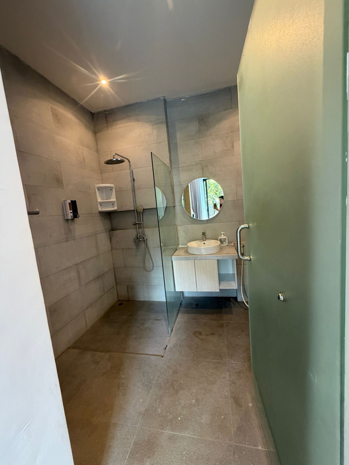 Un baño moderno con cabina de ducha de vidrio, un espejo redondo y un lavabo blanco.
