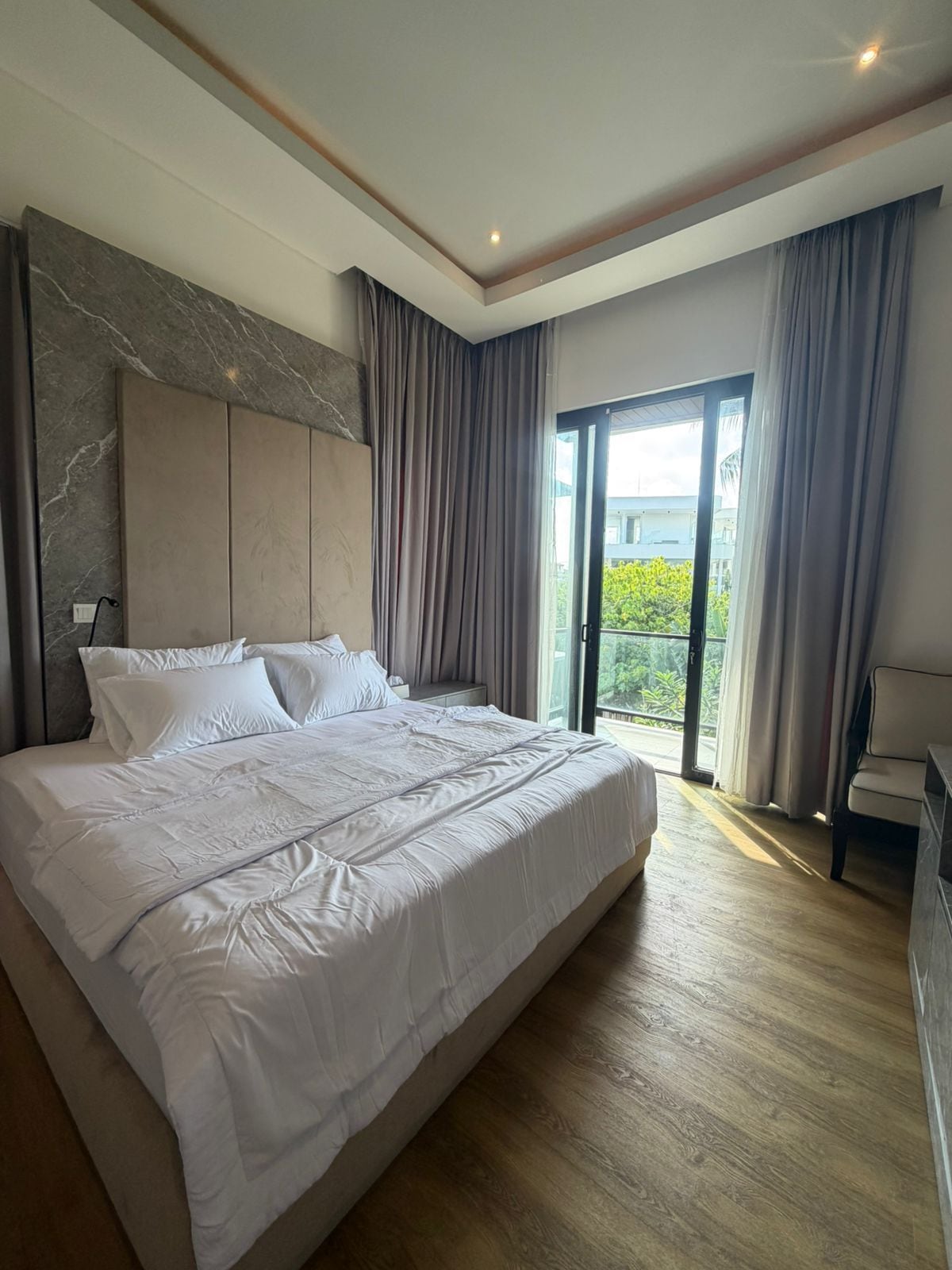 Un dormitorio moderno con una cama grande, cabecera y vistas al exterior a través de un ventanal.