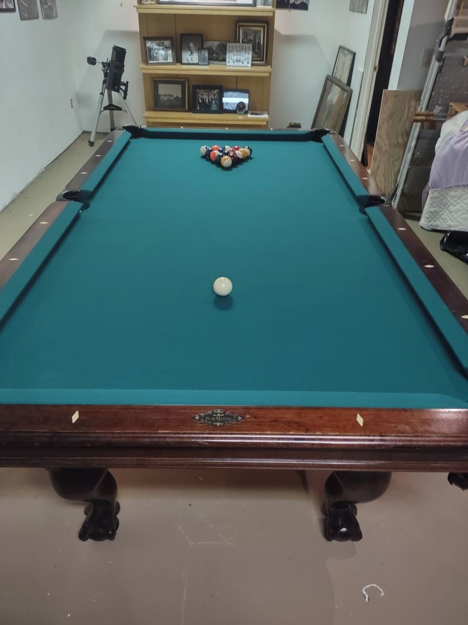 A pool table with balls, a telescope, and a shelf with framed photos.