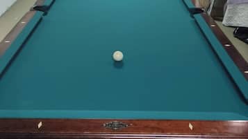 A pool table with balls, a telescope, and a shelf with framed photos.