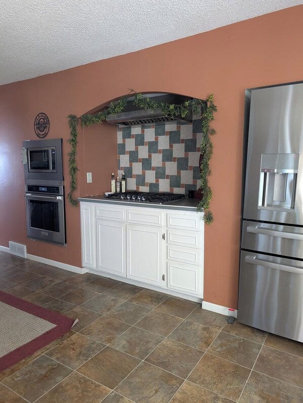 A kitchen with white cabinets, a tiled backsplash, a stainless steel refrigerator, and a microwave.