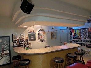 Una zona de bar con mostrador curvo, taburetes y diversas decoraciones, incluyendo cuadros enmarcados y botellas.