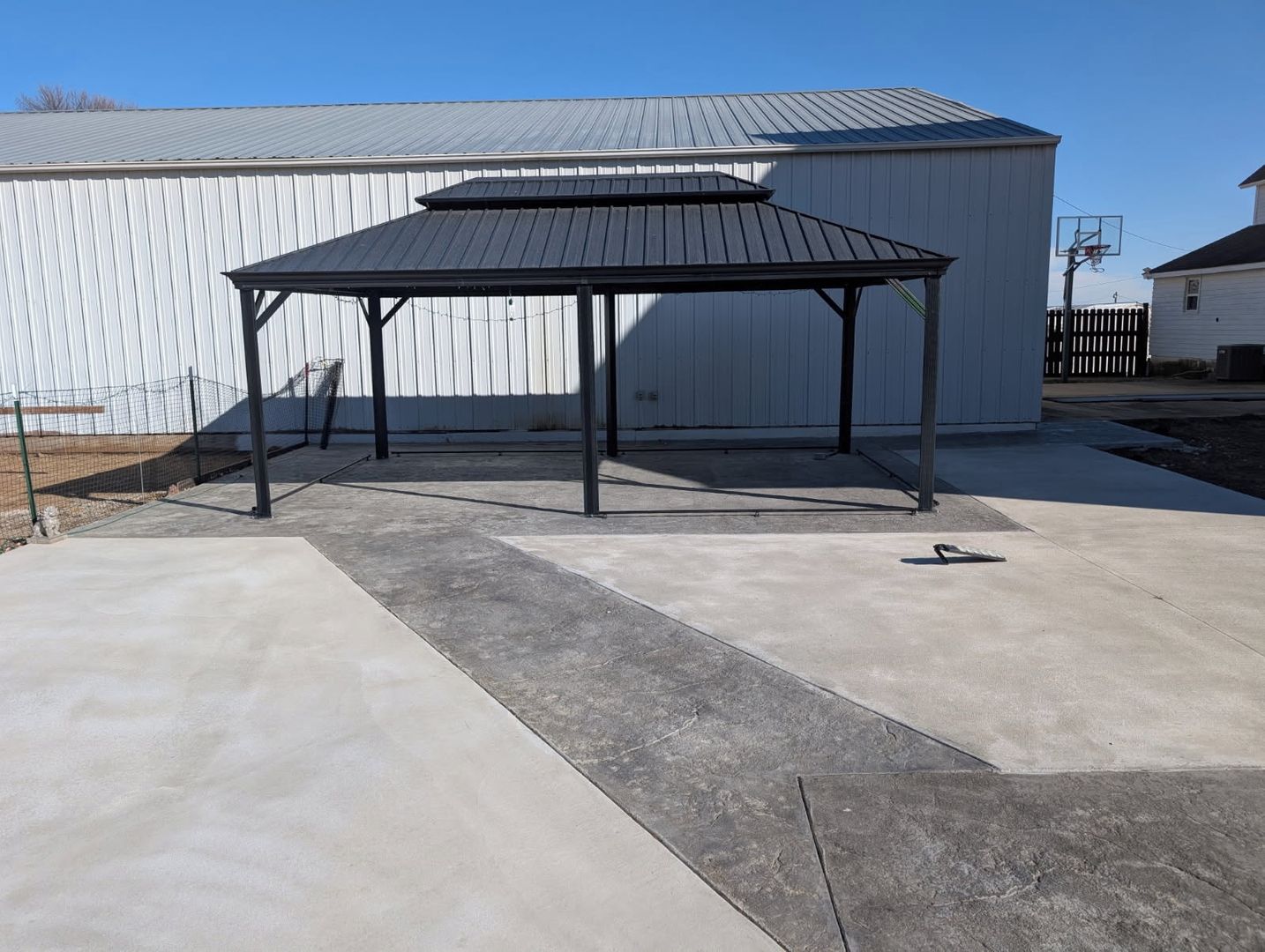 A covered patio area with a metal roof and concrete flooring, adjacent to a white building with a corrugated metal exterior.