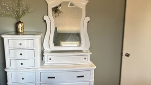A bedroom with a white dresser, a mirror, a vase with flowers, and a bed with a blue cover. - Bed and Breakfast • King Bed + Game Room + Fire Pit (Kiron)