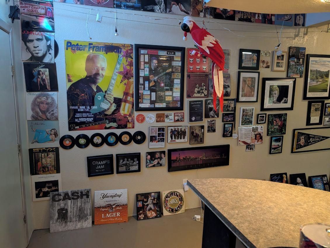 Una pared decorada con carteles enmarcados, fotografías y discos de vinilo, con un loro colgando del techo.