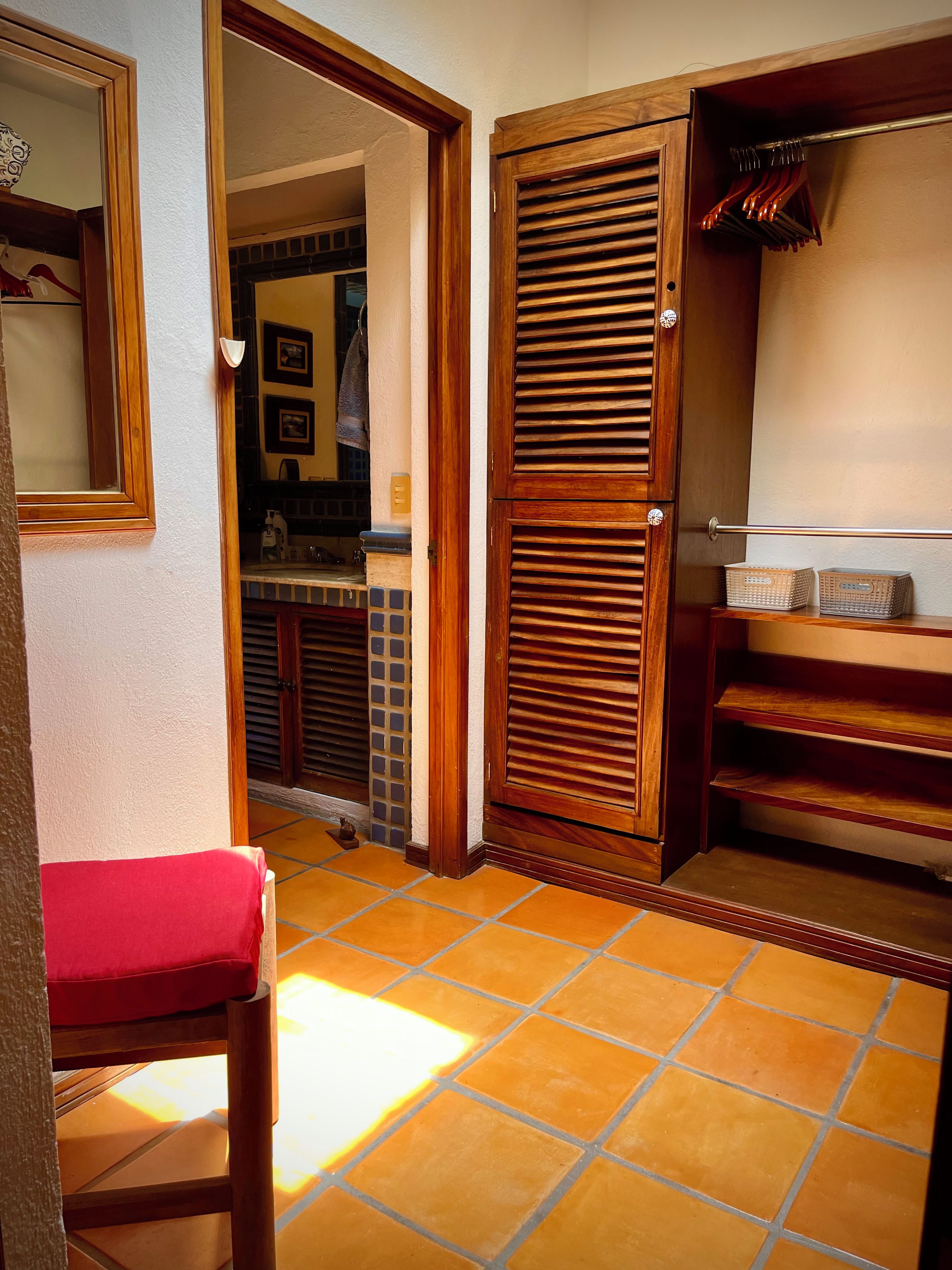Un couloir avec une porte en bois, une chaise rouge et un sol carrelé.