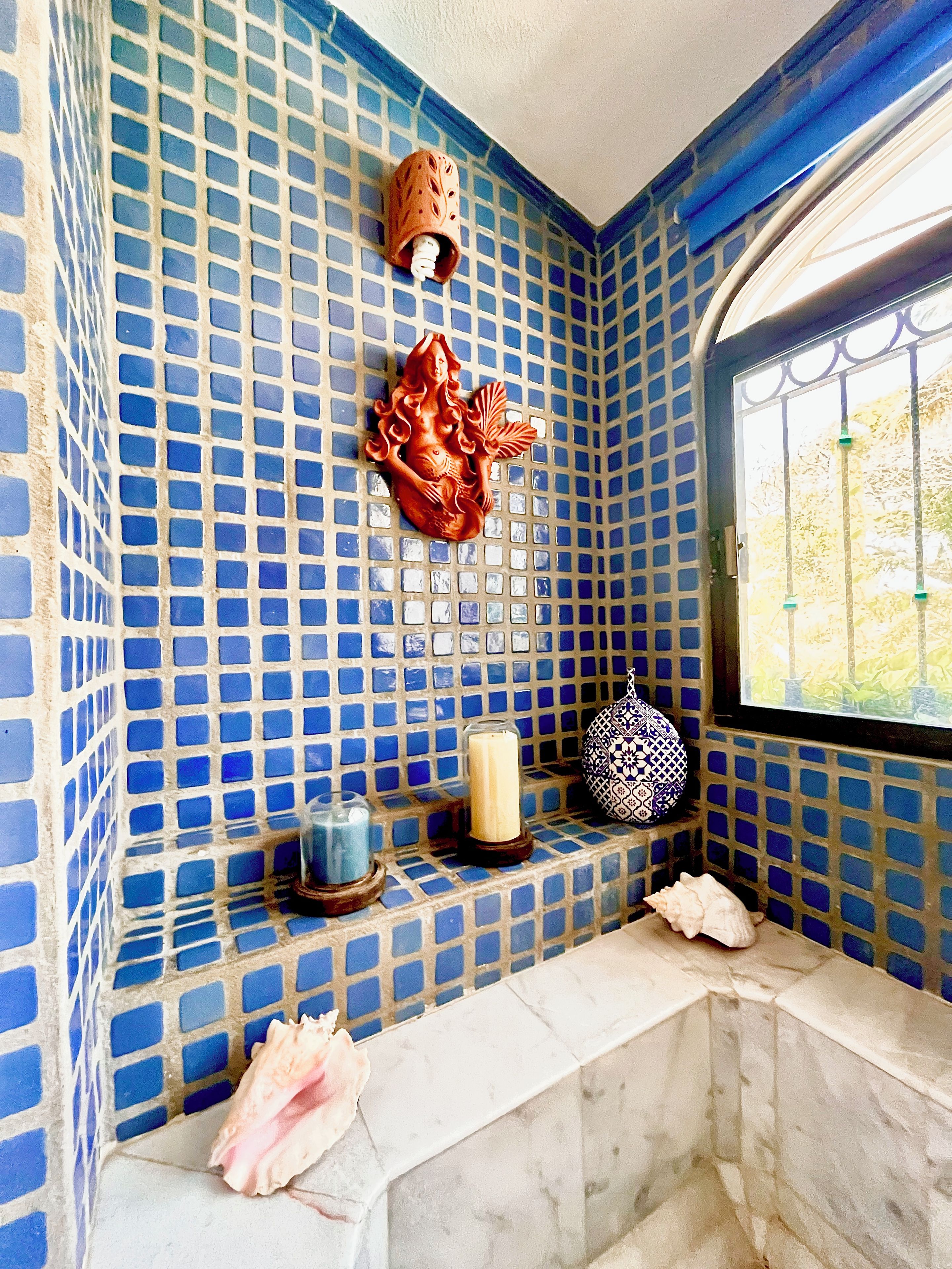 Ein Badezimmer mit blauen Mosaikfliesen, einem Wanddekor, einer Kerze und einer Vase auf einem Regal.