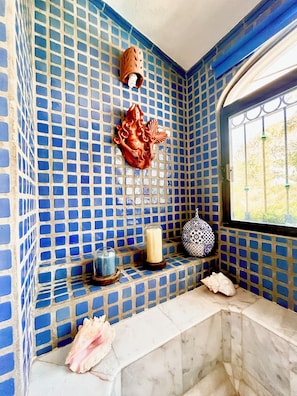 A bathroom with blue mosaic tiles, a decorative wall piece, a candle, and a vase on a shelf.