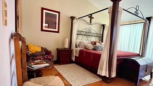 Ein Schlafzimmer mit einem Himmelbett, einem Holzstuhl, einem Nachttisch und einem Deckenventilator.