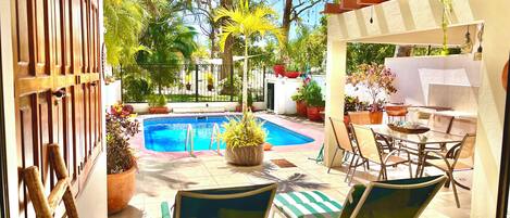 A pool area with lounge chairs, a table, and potted plants.