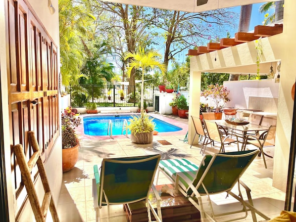A pool area with lounge chairs, a table, and potted plants.