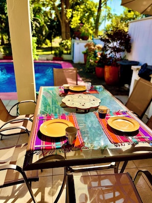 An outdoor dining area with a glass table, chairs, and a pool in the background. - Delightful 3-bedroom house with pool, AC near Marina & Beach in Puerto Vallarta (Puerto Vallarta)