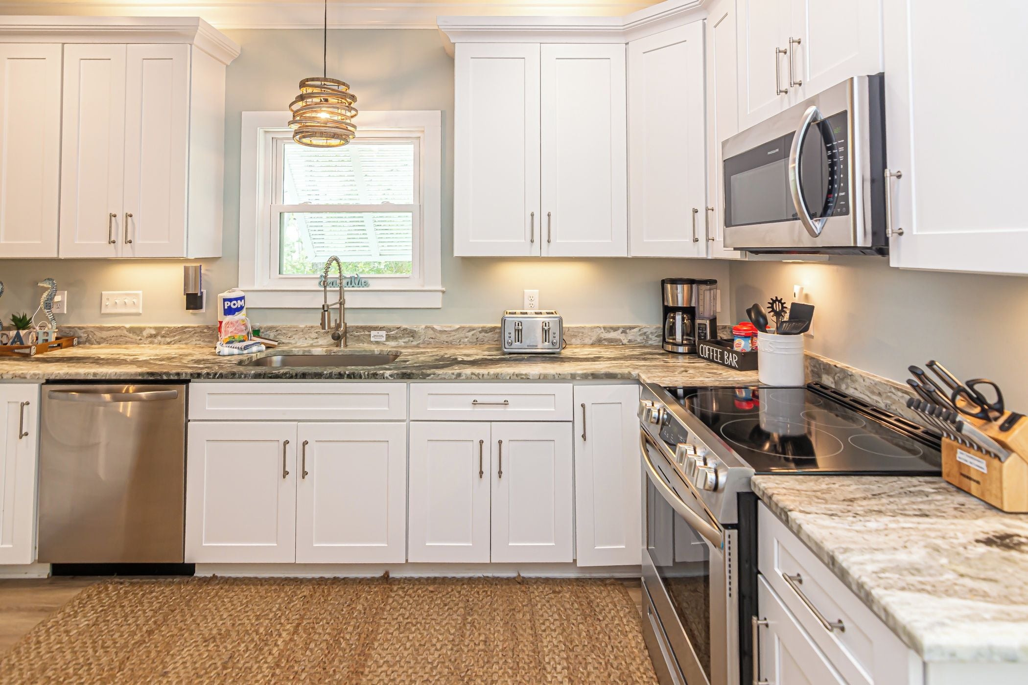 A modern kitchen with white cabinets, a granite countertop, a built-in dishwasher, a stainless steel range, and a coffee station.