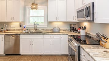 A modern kitchen with white cabinets, a granite countertop, a built-in dishwasher, a stainless steel range, and a coffee station.