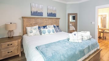 Una cama bien hecha con una manta azul, una mesita de noche de madera con una lámpara y dos cuadros colgados en la pared.