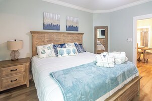 Una cama bien hecha con una manta azul, una mesita de noche de madera con una lámpara y dos cuadros colgados en la pared.