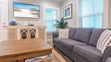 Una sala de estar con una mesa de comedor de madera, un sofá gris y un televisor mostrando una escena de playa.