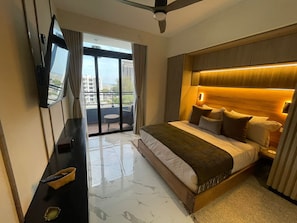 A hotel room with a large bed, a flat-screen TV mounted on the wall, a balcony with a table and chairs, and a ceiling fan. - Urban Oasis Ocean-View Studio with Balcony (Santo Domingo)