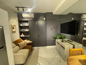 A modern living room with a sofa, a dining table, and a flat-screen TV. - Cozy Ocean View Retreat for Couples • Balcony, Pool & Gym • Gazcue (Santo Domingo)
