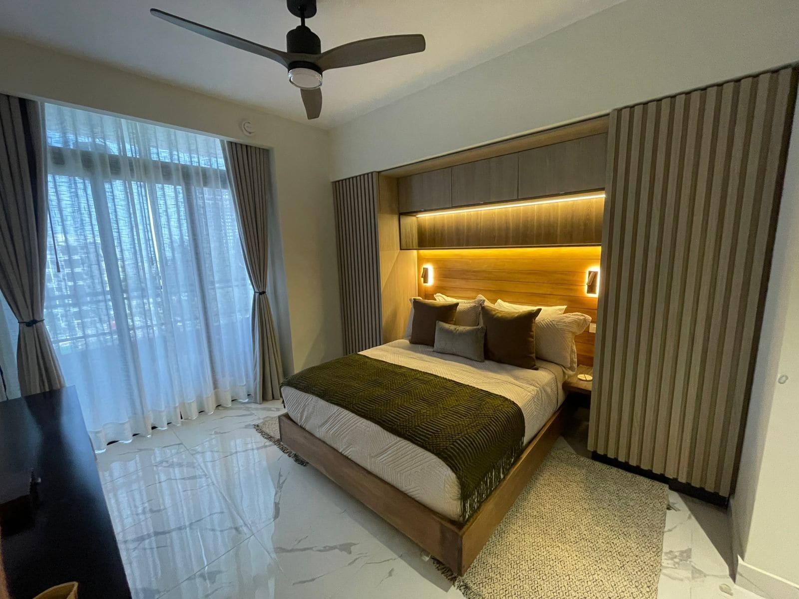 Une chambre moderne avec un lit, des rideaux, un ventilateur de plafond et une vue sur la ville.