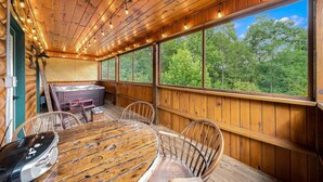Eine Holzterrasse mit Whirlpool, Esstisch und Stühlen, mit Blick auf ein bewaldetes Gebiet.
