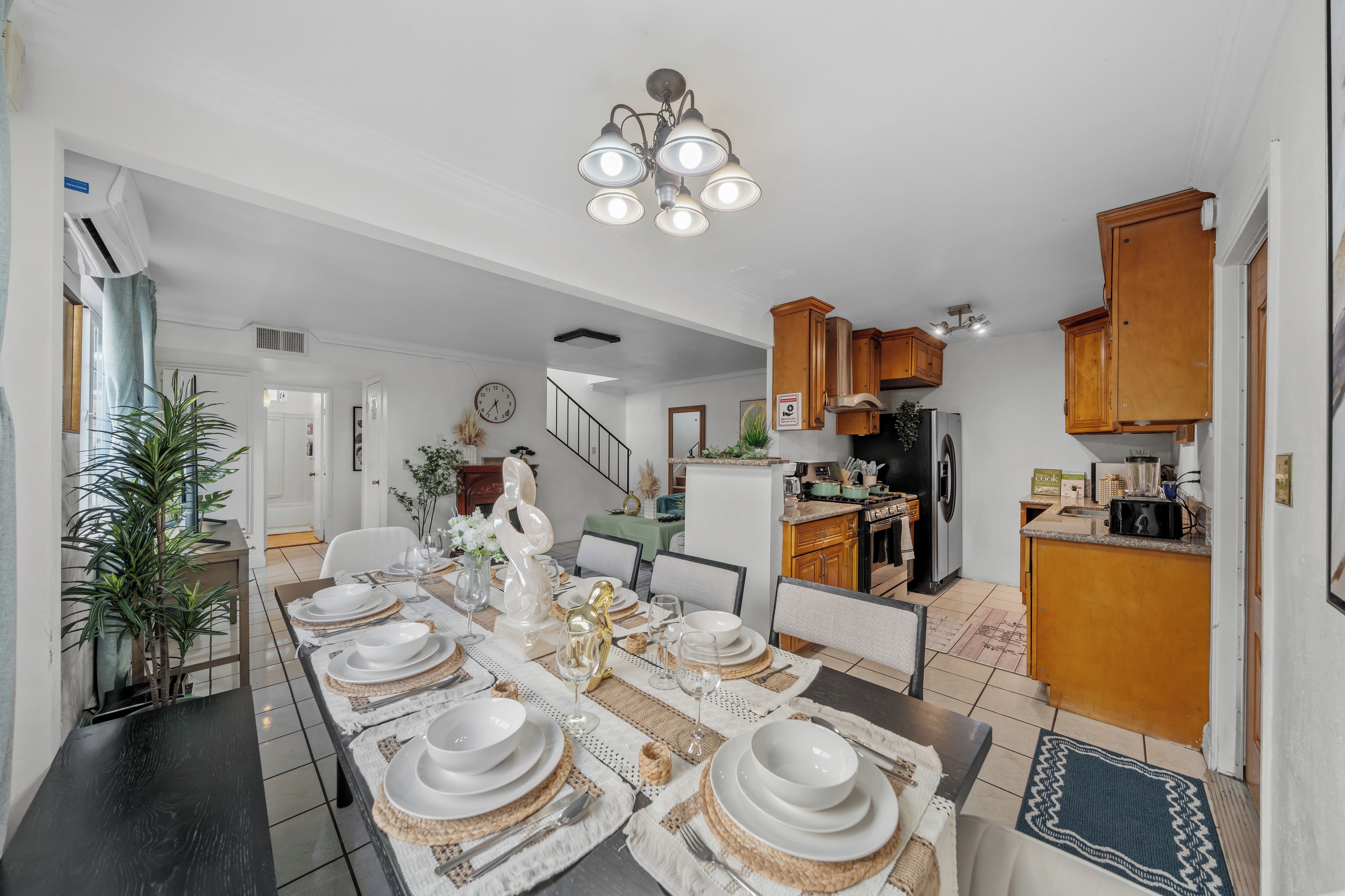 Comedor con una larga mesa dispuesta para una comida, una cocina al fondo y una escalera que sube a otro nivel.
