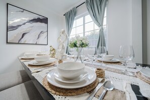 A dining table set with white plates, bowls, and cutlery, with a vase of white flowers and a decorative sculpture. - Garage, Gated Yard, near SD Gaslamp, DT, 4BR/2Bth (National City)