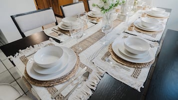 A dining table set with white plates, bowls, and glasses, with a woven placemat and a vase of flowers.