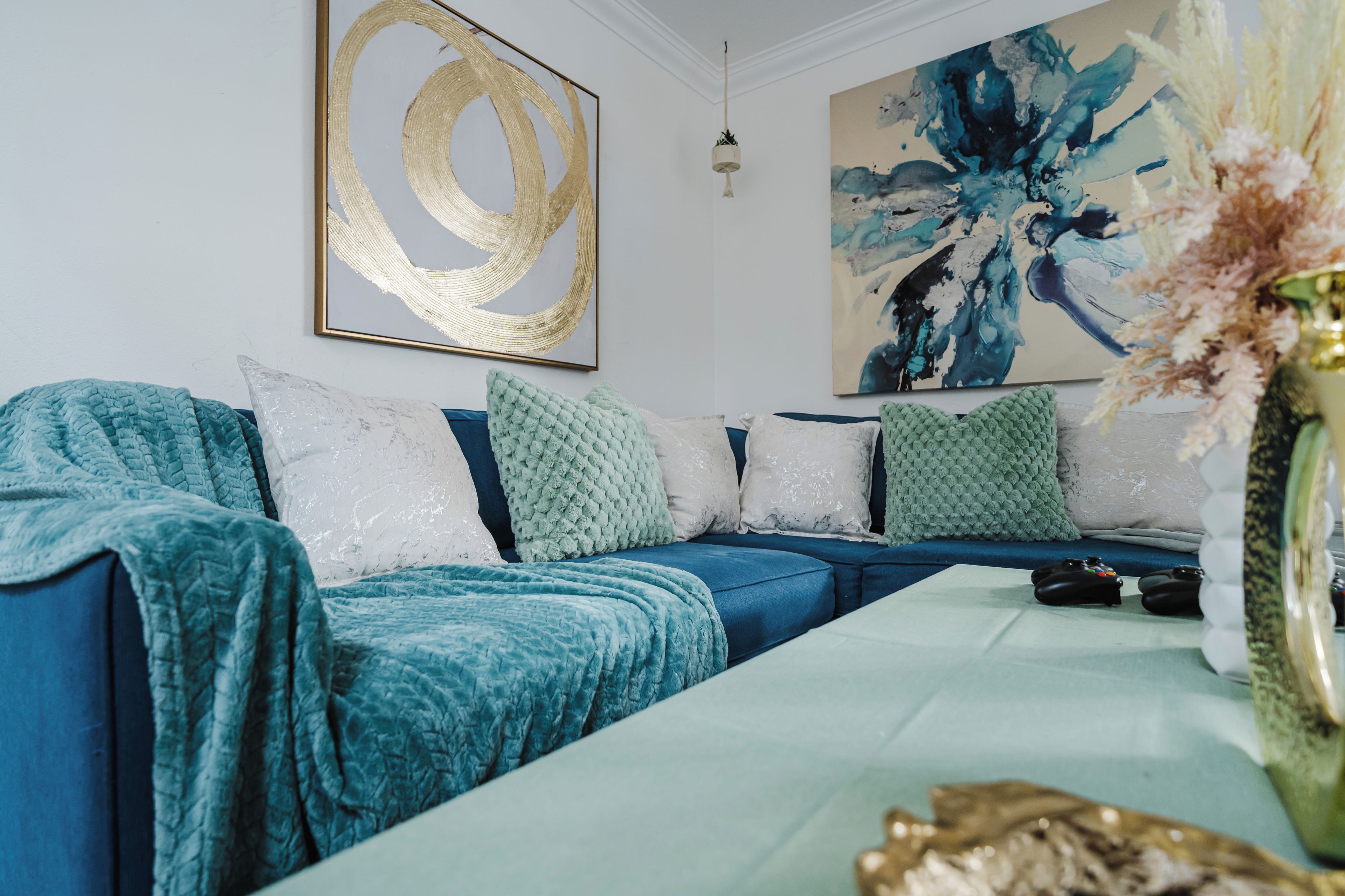 Un salon moderne avec un canapé bleu, un vase décoratif et des tableaux abstraits accrochés au mur.