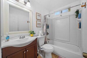 A bathroom with a white sink, toilet, and bathtub. There are framed pictures on the wall, a potted plant on the sink, and toiletries on the countertop. - Garage, Gated Yard, near SD Gaslamp, DT, 4BR/2Bth (National City)