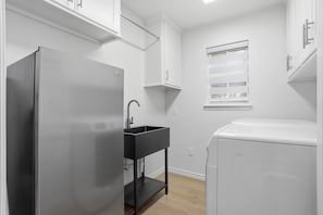 A compact kitchen with a stainless steel refrigerator, a black sink, and a white washing machine. - Tranquil Retreat - 3BR/3BA - Centrally Located (Lubbock)