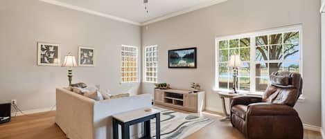 A living room with a ceiling fan, a sofa, a recliner, a coffee table, a TV, and a window with a view.