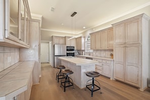 A modern kitchen with a central island, bar stools, stainless steel appliances, and light wood cabinetry. - Tranquil Retreat - 3BR/3BA - Centrally Located (Lubbock)