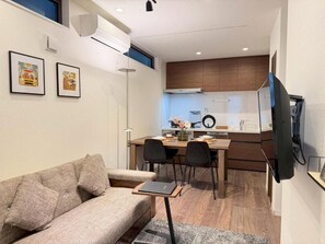 A modern living room with a sofa, a dining table with chairs, a kitchen area with a refrigerator, and a flat-screen TV mounted on the wall. - NIKYO Taisho BLA Private Villa OSAKA (Osaka)
