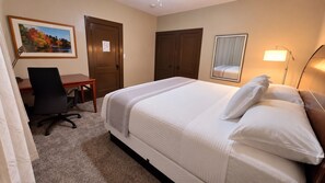 Ein Hotelzimmer mit Bett, Schreibtisch, Stuhl, Tür und einem gerahmten Bild an der Wand.