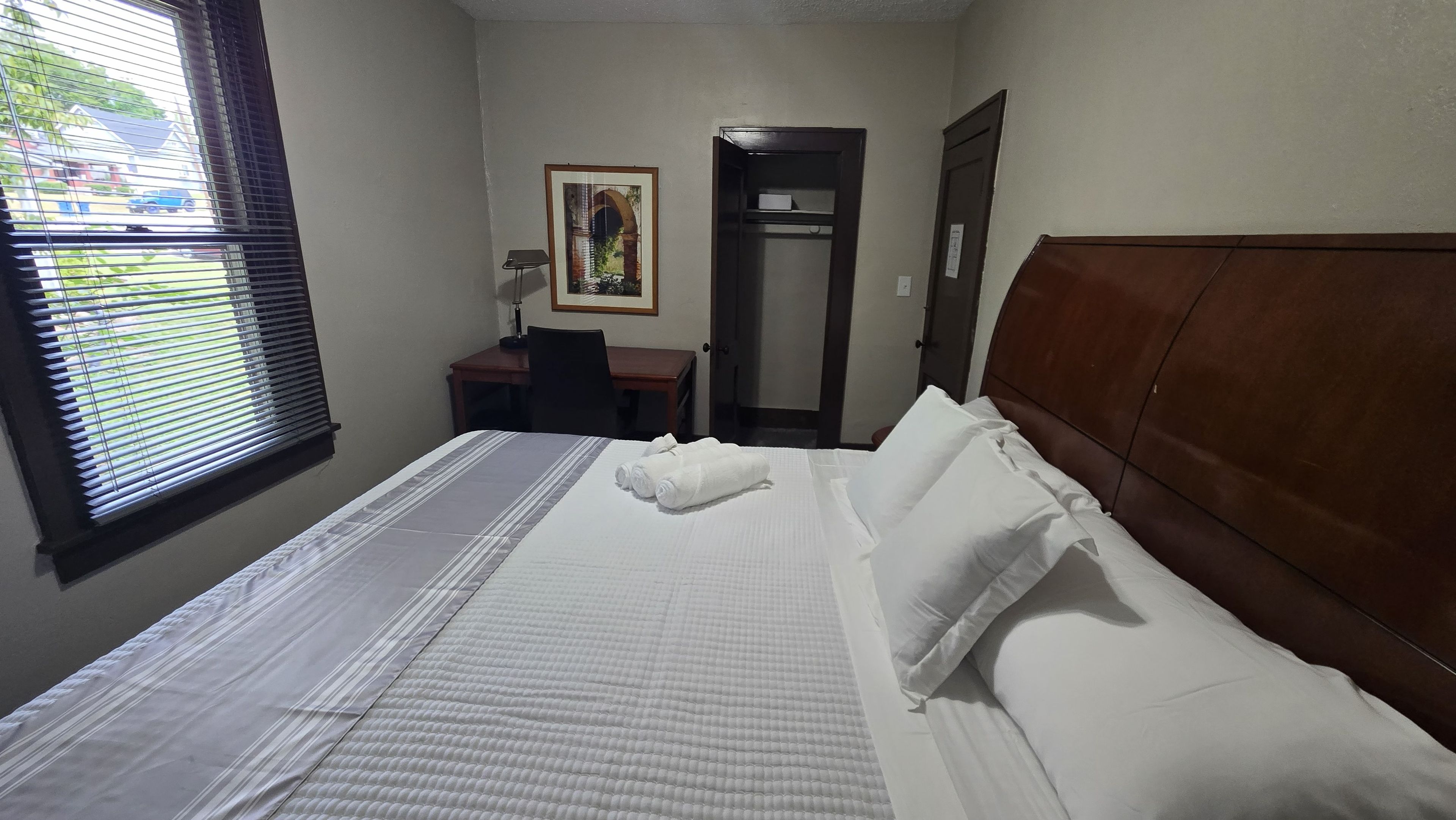 Ein Hotelzimmer mit Bett, Schreibtisch, Stuhl, Tür und einem Fenster mit Jalousien.