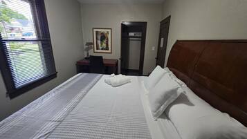 Ein Hotelzimmer mit Bett, Schreibtisch, Stuhl, Tür und einem Fenster mit Jalousien.