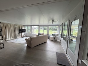 Een ruime woonkamer met een grote bank, een televisie en uitzicht op de omgeving door grote ramen.