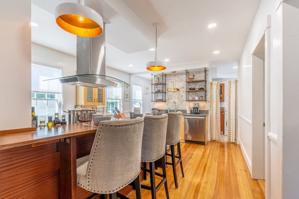 A modern kitchen with a bar area, wooden flooring, and pendant lighting.