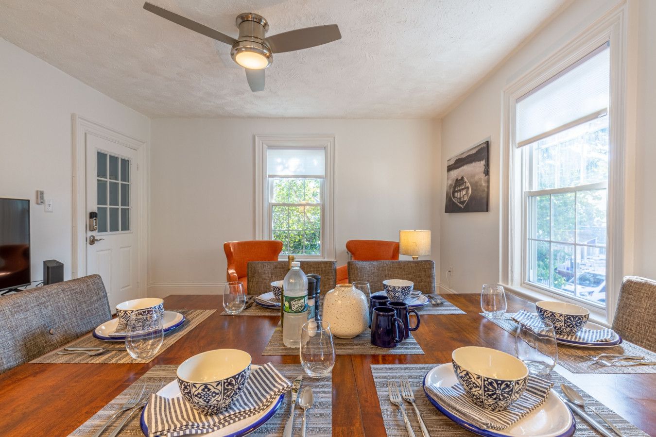 Un coin repas avec une table en bois dressée pour six personnes, entourée de chaises, et un ventilateur de plafond au-dessus.