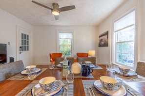A dining area with a wooden table set for six, surrounded by chairs, and a ceiling fan above.