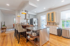 A modern kitchen with a central island, wooden flooring, and pendant lighting.