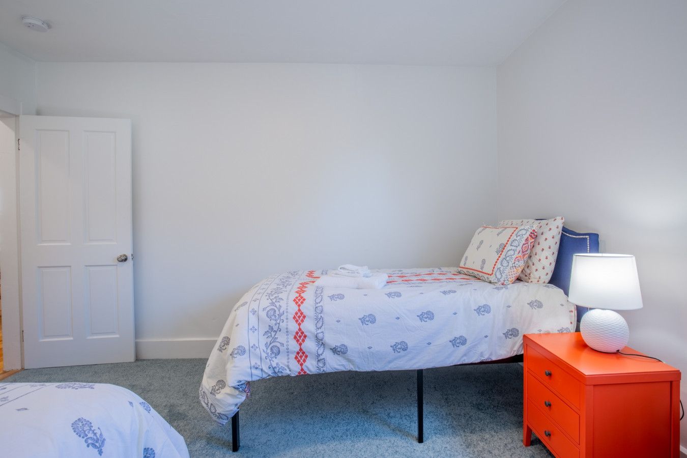 A bedroom with a bed, a nightstand, a lamp, and a door.