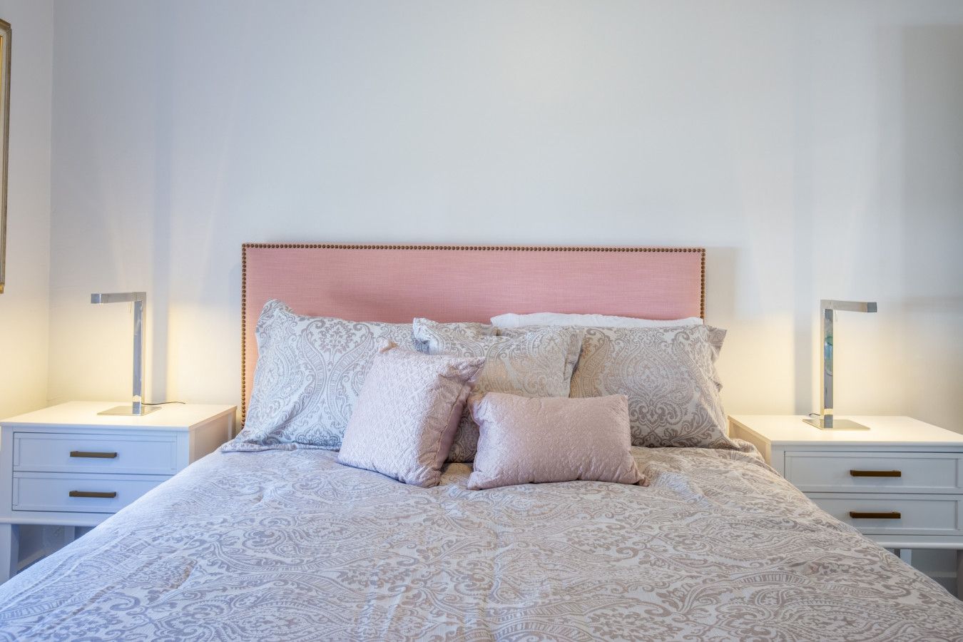 Un lit bien fait, recouvert d’une couvre-lit à motifs et agrémenté de plusieurs coussins, avec de chaque côté des tables de chevet sur lesquelles sont posées des lampes.