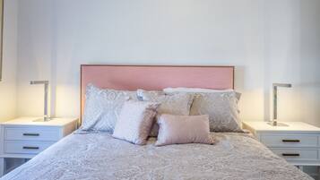 Un lit bien fait, recouvert d’une couvre-lit à motifs et agrémenté de plusieurs coussins, avec de chaque côté des tables de chevet sur lesquelles sont posées des lampes.