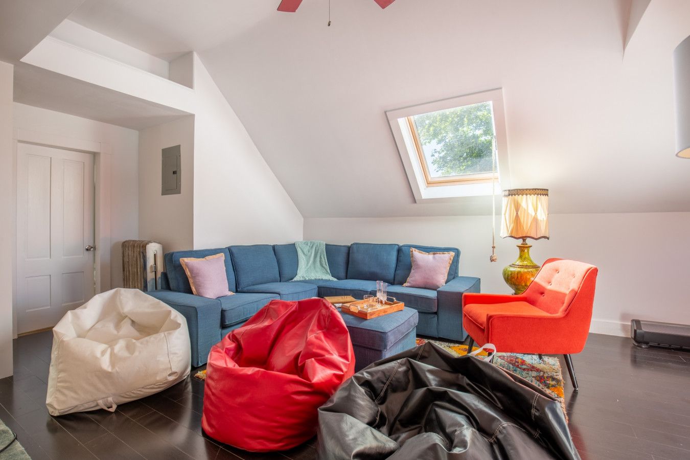 Un salon avec un canapé bleu, un fauteuil rouge, une lampe et une fenêtre donnant sur des arbres.
