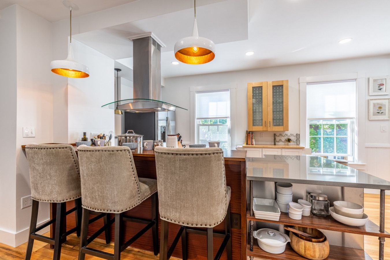 A modern kitchen with a central island, bar stools, pendant lighting, and a view of the outdoors.